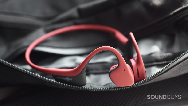The AfterShokz Air bone conduction headphones in red rest on top of a zippered sling.
