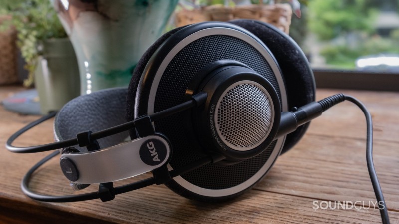 The AKG K702 rests on its side atop a wood surface with a window and plants in the background.