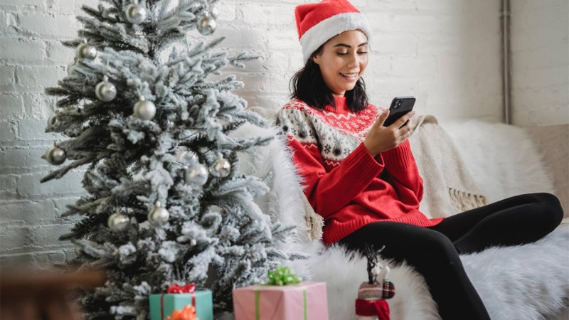 frau-laechelt-smartphone-weihnachten-tannenbaum-geschenke